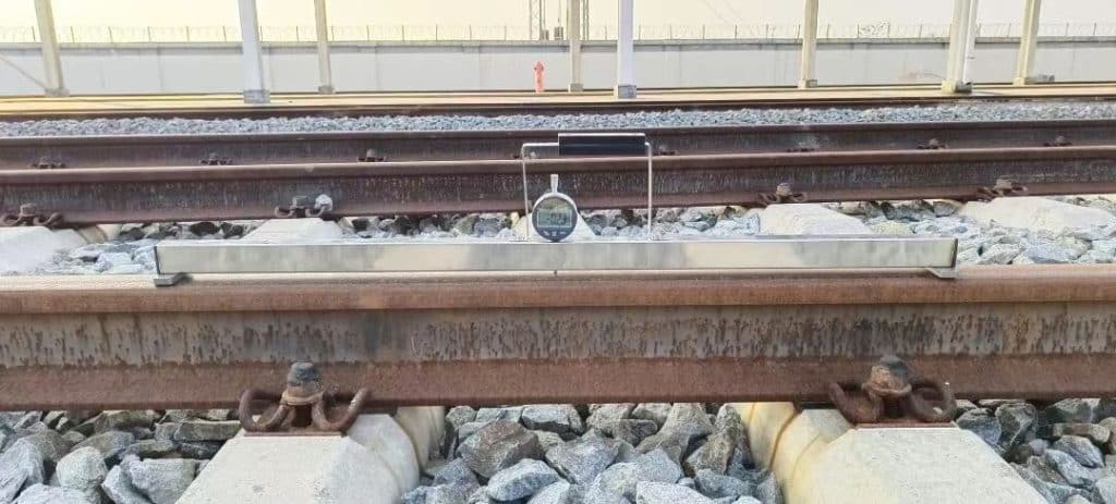 Technician measuring horizontal straightness of crane rail using straight edge