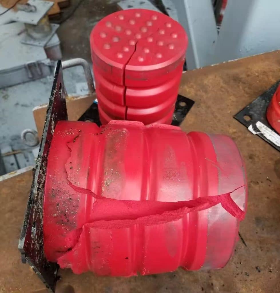 Damaged red multi layer polyurethane crane buffer, cracked and fractured industrial crane travel rubber bumper, worn out lifting machinery safety stop buffer at factory workshop