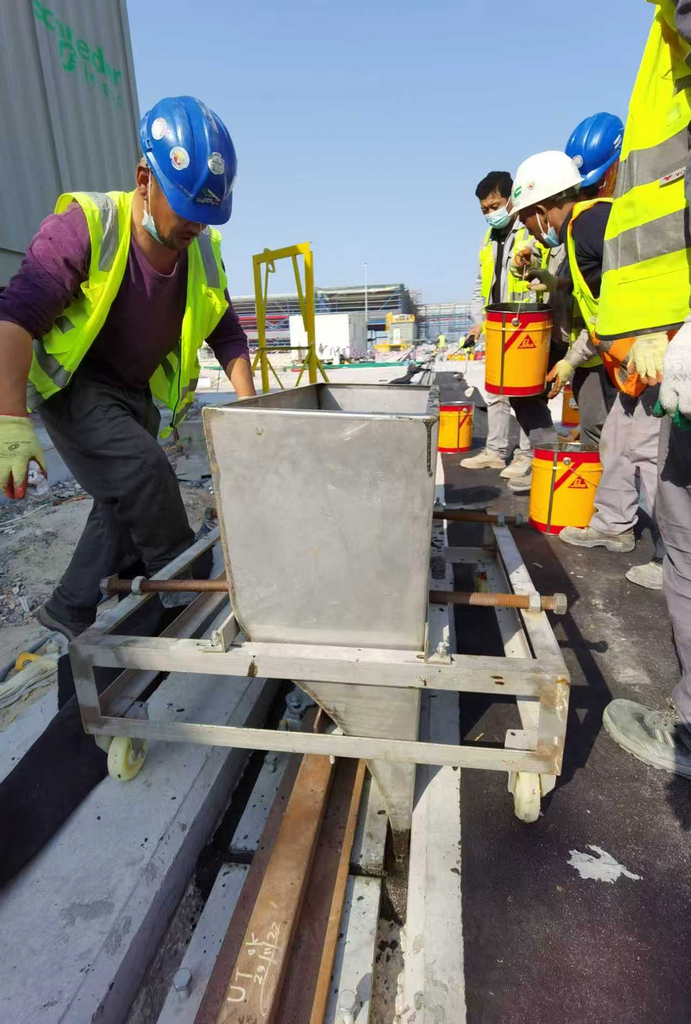 Grouting cart pouring non‑shrink grout into crane rail base gap at port construction site rail foundation grouting
