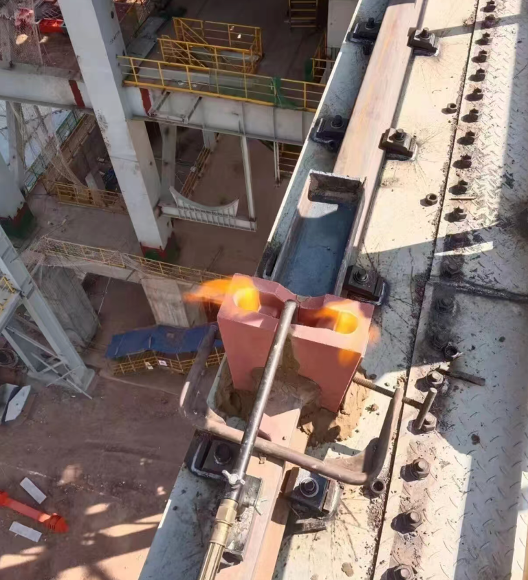 Rail aluminothermic welding pre‑heating operation on crane rail, gas preheater heating rail gap with sand mold assembled, heavy‑duty factory overhead track welding site